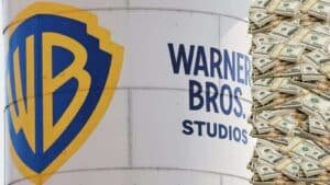 El icónico logotipo de Warner Bros. y el texto 'WARNER BROS. STUDIOS' en el lateral de un tanque de agua o silo, junto a una pila exagerada de fajos de billetes de cien dólares, simbolizando una posible oferta de compra millonaria.