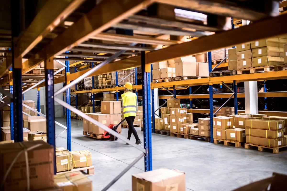 Empleada con un chaleco de seguridad reflectante amarillo 
mientras trabaja dentro de un gran almacén o centro de distribución de Amazon.