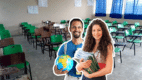Un maestro con un globo terráqueo y una maestra con libros sonriendo frente a un salón de clases vacío para celebrar el Día del Maestro 2026 en México.