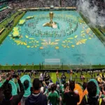 Vista de un estadio de la Copa del Mundo 2026 completamente lleno con miles de aficionados, banderas y una pantalla gigante que ilustra el impacto global y los récords de audiencia de las transmisiones.