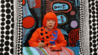 Yayoi Kusama pintando frente a uno de sus característicos fondos llenos de lunares y colores vibrantes
