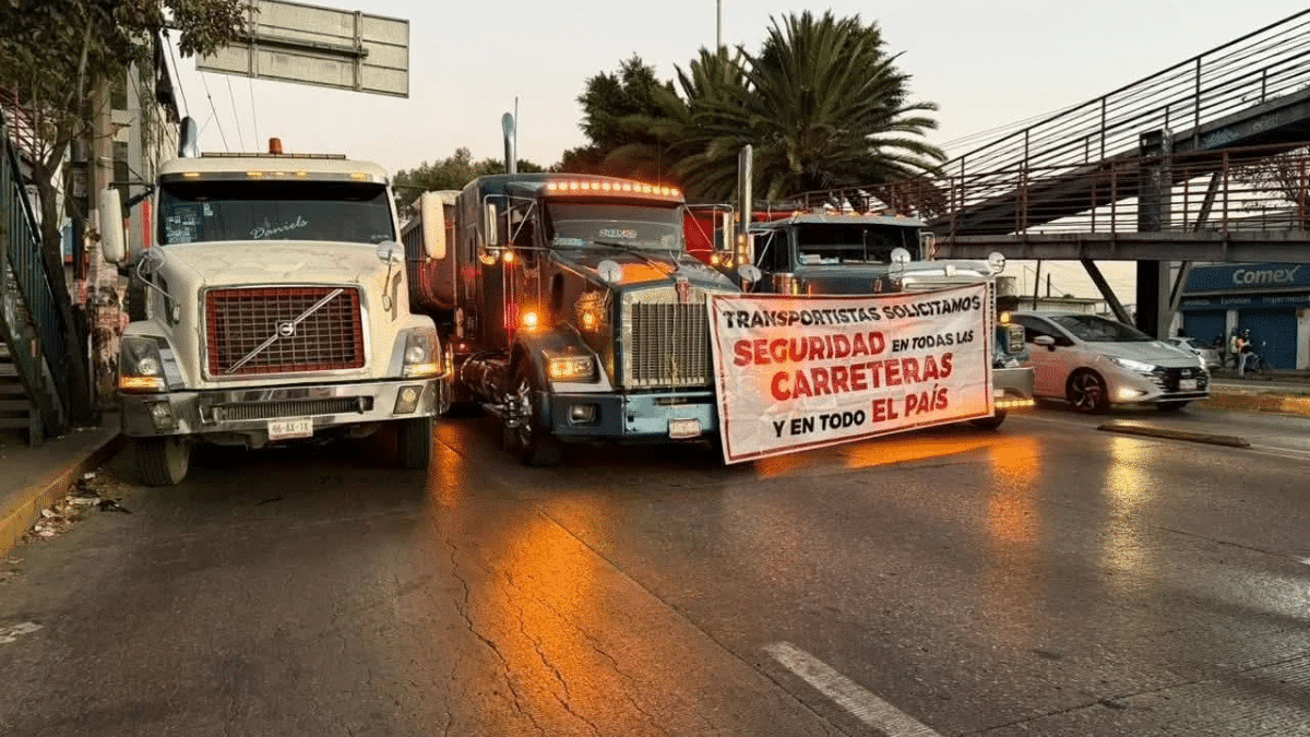 Tráileres de carga estacionados en el acotamiento de una autopista cerca de una caseta de cobro durante el paro de transportistas.
