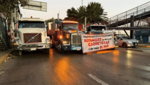Tráileres de carga estacionados en el acotamiento de una autopista cerca de una caseta de cobro durante el paro de transportistas.
